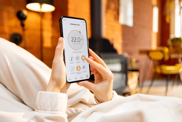 woman holding phone with running smart home application for heating temperature control, while lying relaxed, close-up on device screen